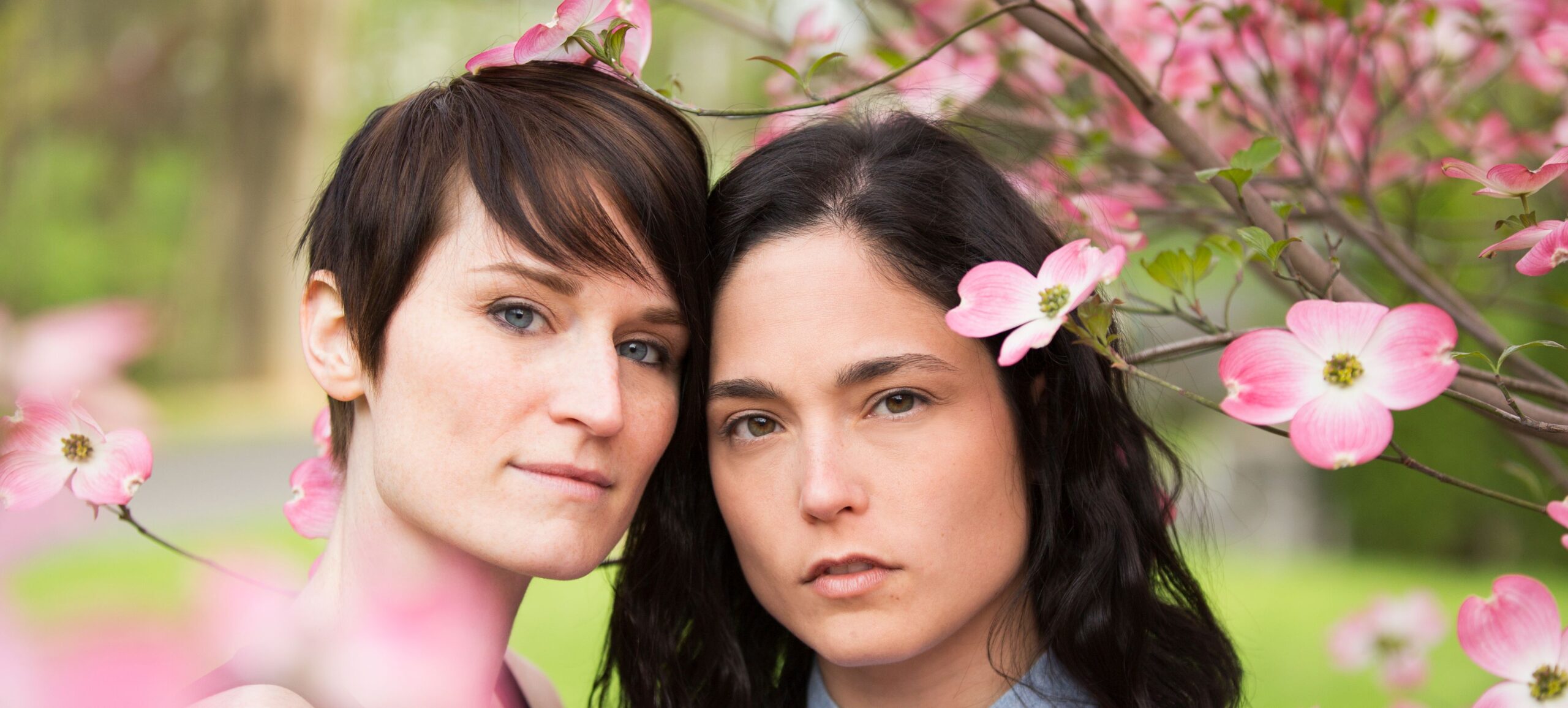 A same sex couple, two women under the branches of a flowering tree. | Gaia